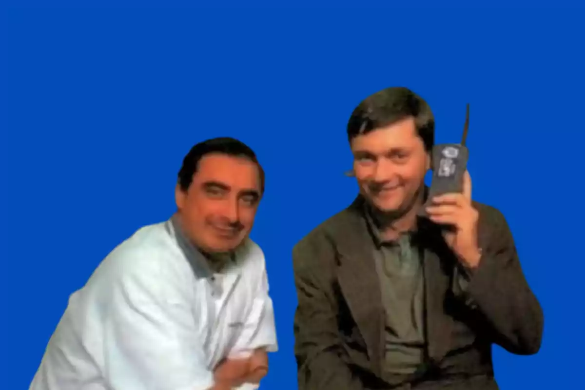 Dos hombres posando, uno de ellos sostiene un teléfono móvil antiguo, con un fondo azul. Dos hombres posando, uno de ellos sostiene un teléfono móvil antiguo, con un fondo azul.