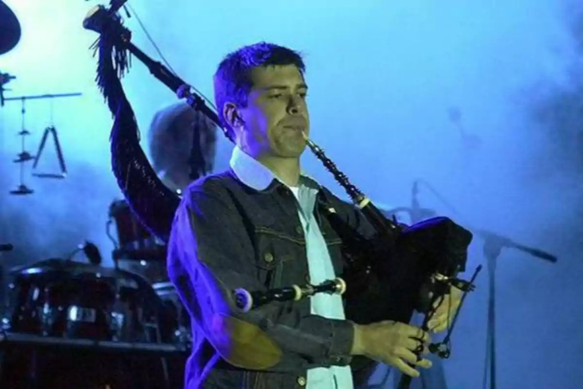 Un hombre tocando la gaita en un escenario con luces azules y humo de fondo.