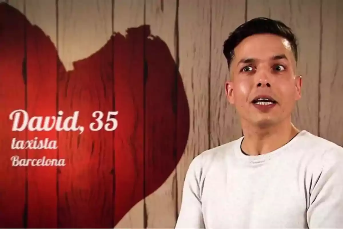 Un hombre con camiseta blanca está frente a un fondo de madera con un corazón rojo.