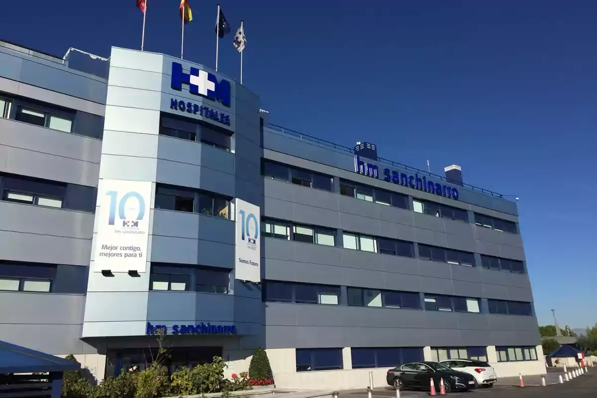 Edificio moderno de un hospital con varias banderas en el techo y carteles conmemorativos en la fachada.