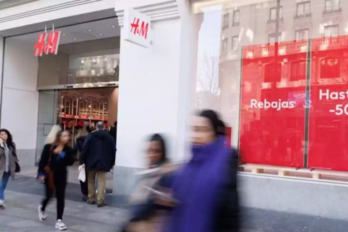 Personas caminando frente a una tienda H&M con un cartel de rebajas en la ventana.