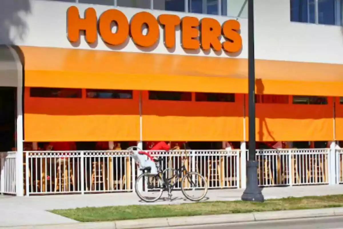 Fachada de un restaurante Hooters con toldos naranjas y una bicicleta estacionada en la acera Fachada de un restaurante Hooters con toldos naranjas y una bicicleta estacionada en la acera