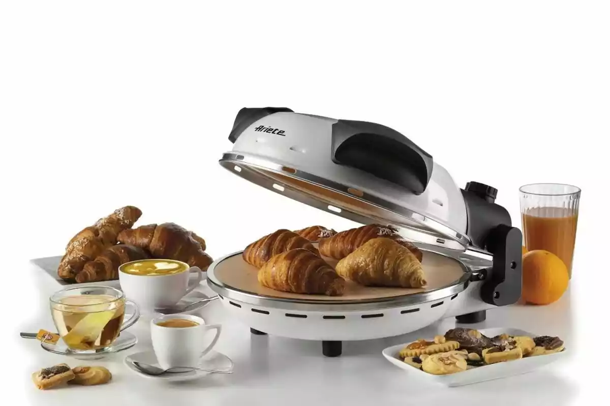 Un horno eléctrico de Lidl con varios croissants dorados en su interior, acompañada de tazas de café, té, un vaso de jugo de naranja, una naranja entera y platos con galletas y más croissants sobre una mesa blanca. Un horno eléctrico de Lidl con varios croissants dorados en su interior, acompañada de tazas de café, té, un vaso de jugo de naranja, una naranja entera y platos con galletas y más croissants sobre una mesa blanca.