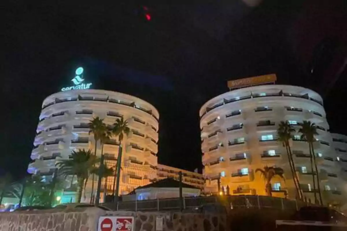 Edificios circulares iluminados por la noche con palmeras en primer plano.