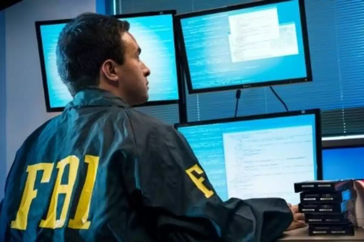 Agente del FBI trabajando en una oficina frente a múltiples monitores de computadora.