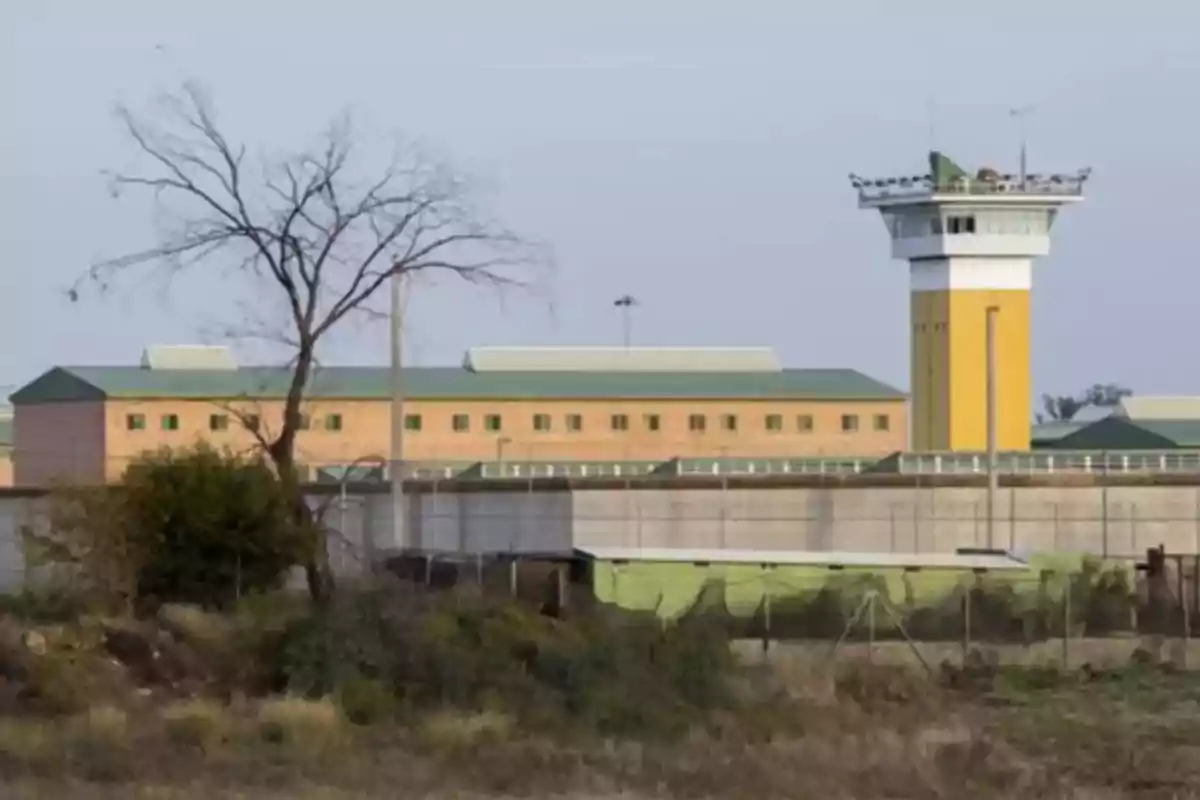 Vista de una prisión con una torre de vigilancia y edificios rodeados por una cerca de seguridad.