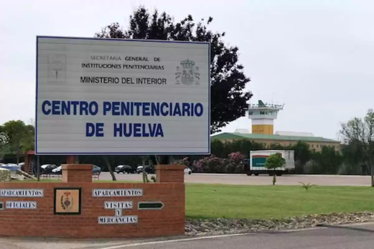 Cartel del Centro Penitenciario de Huelva con una torre de vigilancia en el fondo.