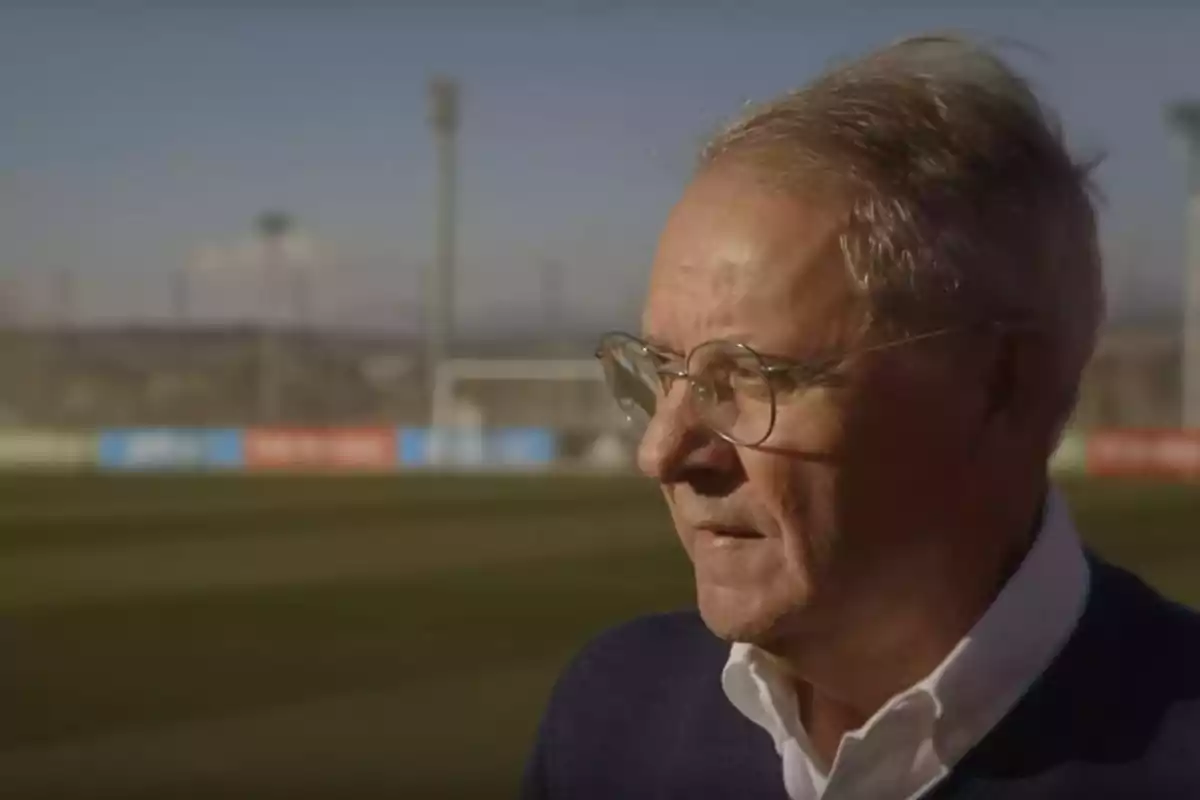 Un hombre mayor con gafas de pie en un campo de fútbol bajo un cielo despejado. Un hombre mayor con gafas de pie en un campo de fútbol bajo un cielo despejado.