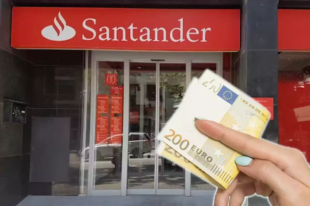 Una mano sosteniendo billetes de 200 euros frente a una sucursal del banco Santander.