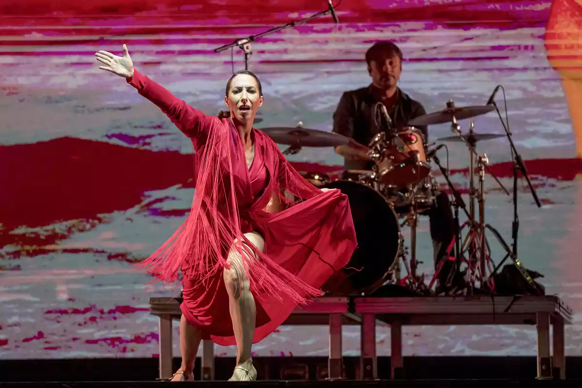 Bailarina de flamenco en un escenario con fondo rojo y baterista al fondo.