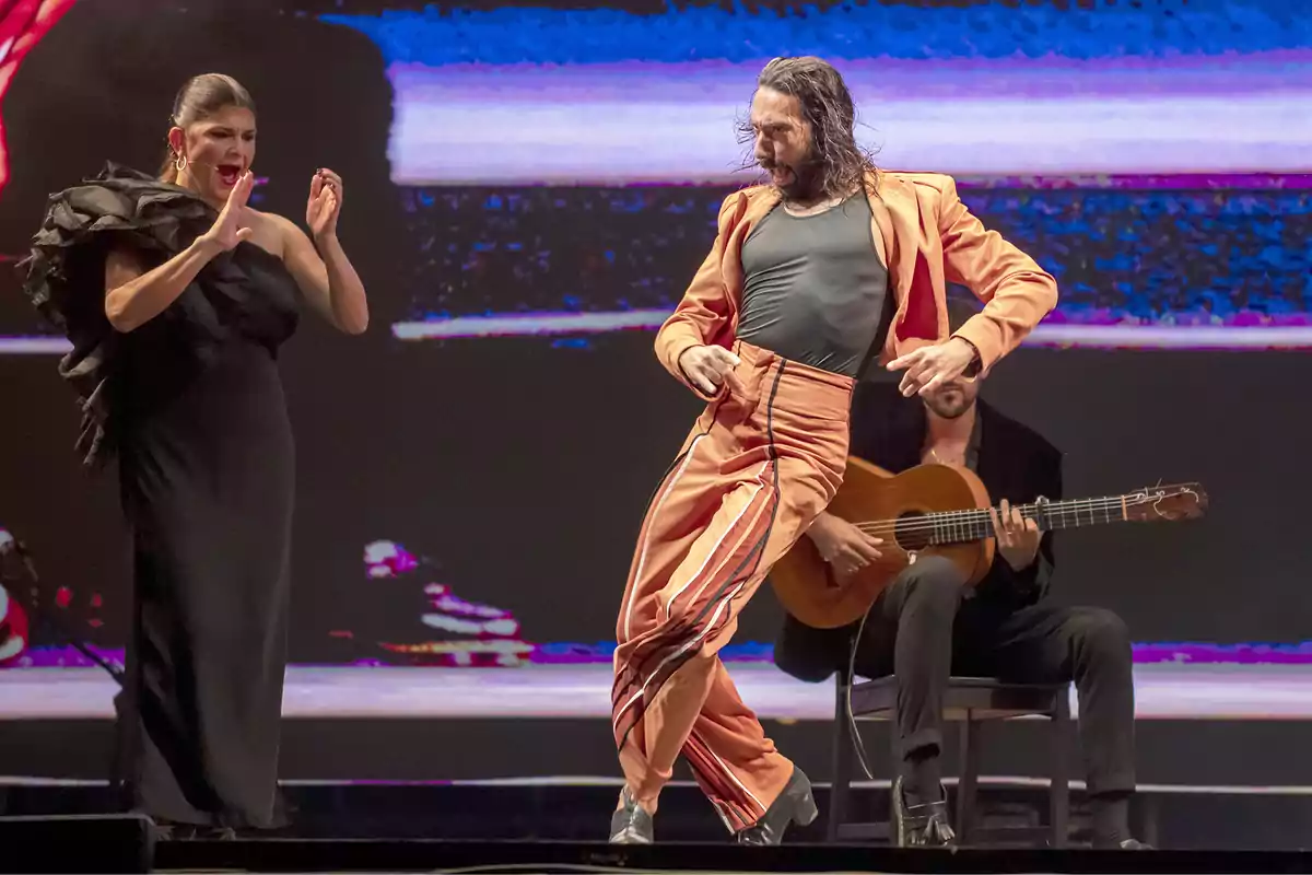 Un hombre baila flamenco con energía mientras una mujer canta y un guitarrista toca en el escenario.