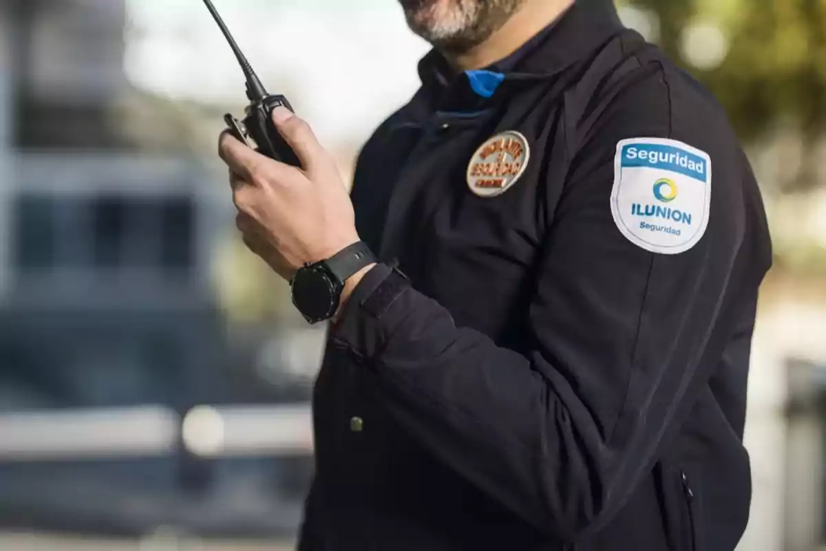 Un guardia de seguridad con uniforme negro sosteniendo un walkie-talkie.