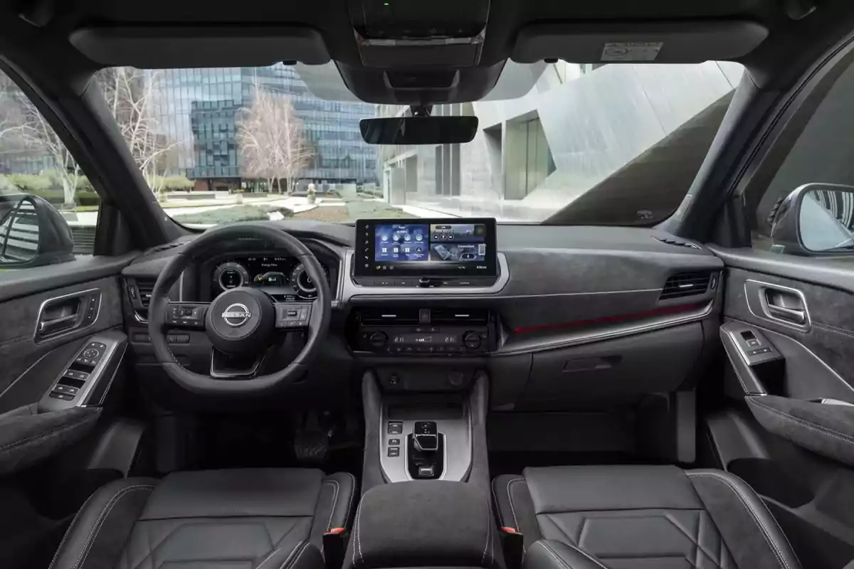 Interior de un Nissan Qashqai e-POWER 2025 moderno con volante multifuncional, pantalla táctil central y asientos de cuero, con un edificio de fondo visible a través del parabrisas. Interior de un Nissan Qashqai e-POWER 2025 moderno con volante multifuncional, pantalla táctil central y asientos de cuero, con un edificio de fondo visible a través del parabrisas.