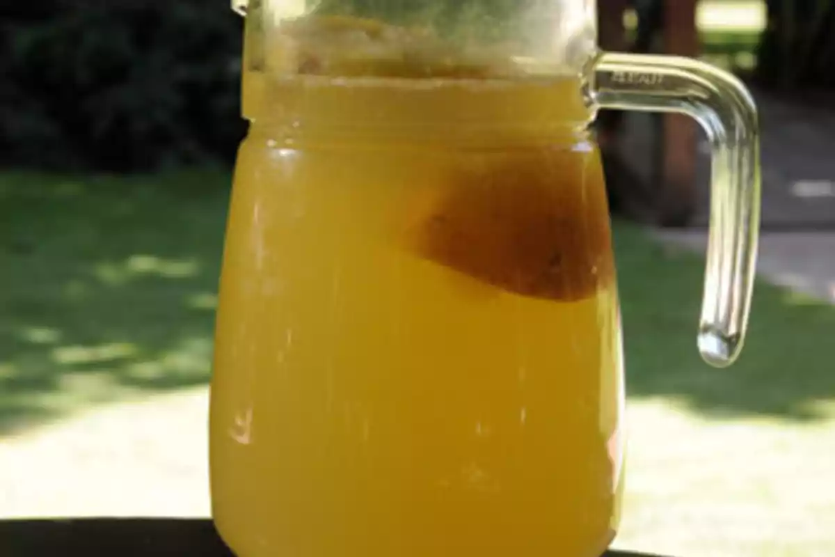 Jarra de vidrio con bebida amarilla y una rodaja de fruta en su interior.
