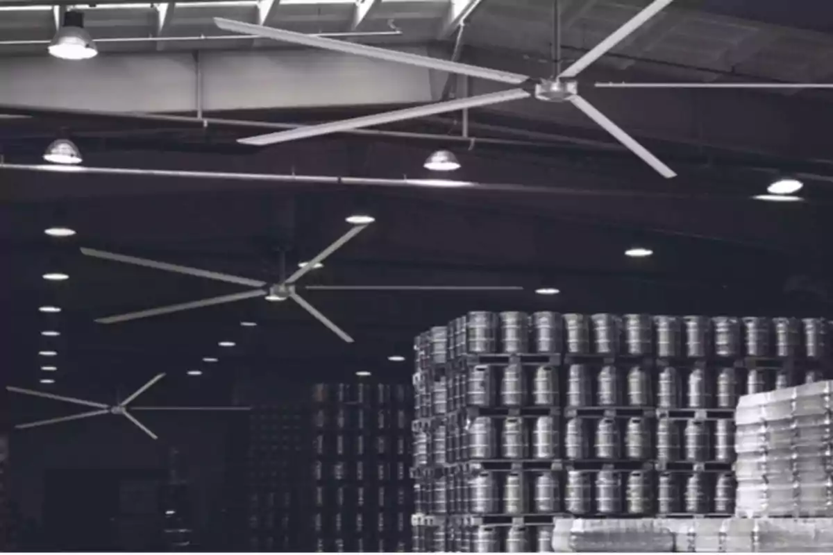 Ventiladores de techo grandes en un almacén con barriles apilados.