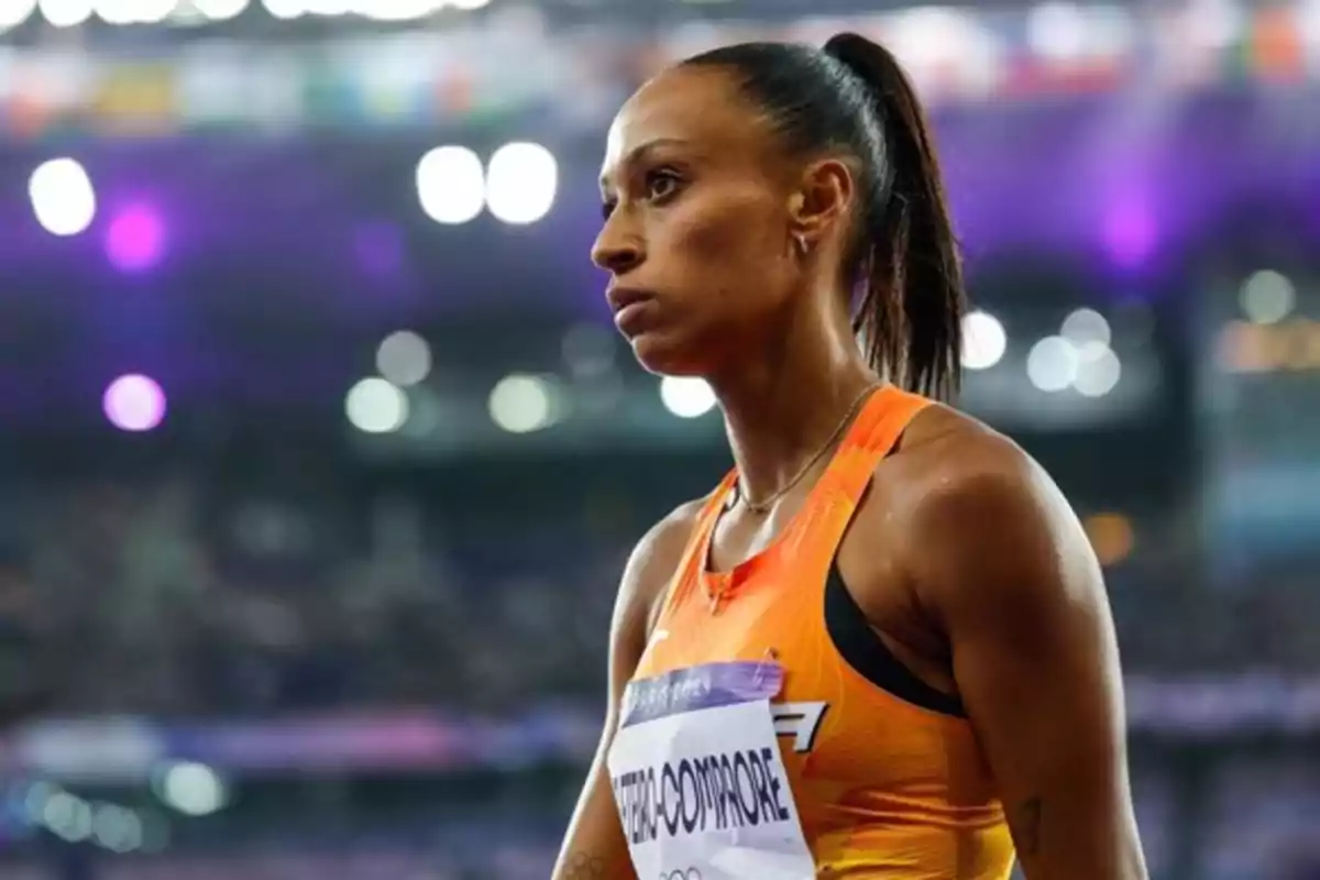 Atleta en una pista de atletismo con un uniforme naranja y un fondo de luces brillantes.