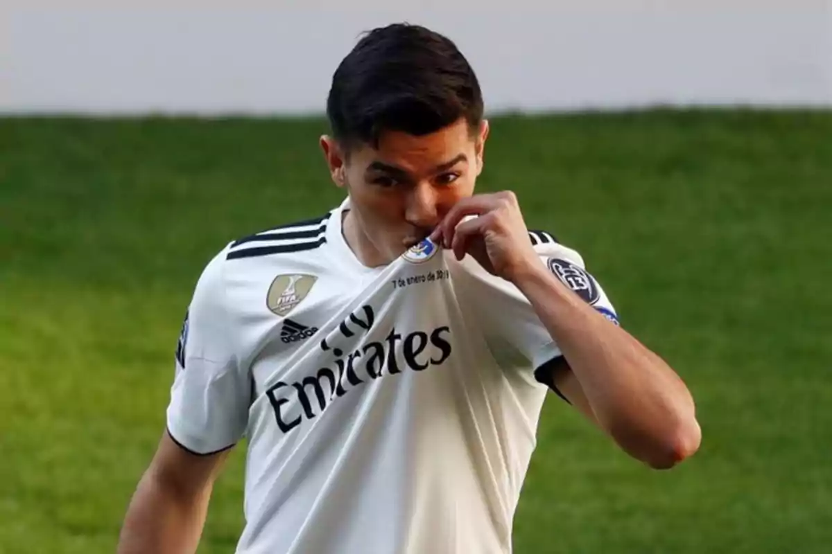 Un jugador de fútbol besa el escudo de su camiseta blanca en el campo.