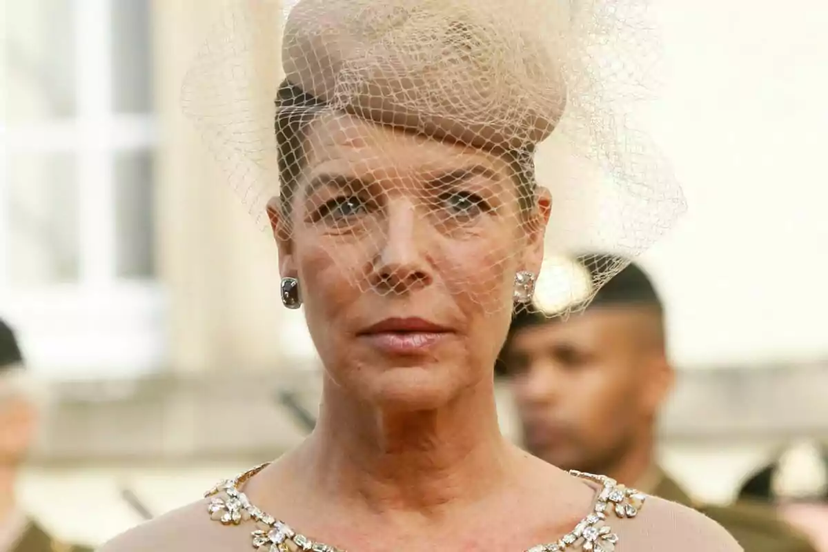 Una persona con un elegante sombrero beige adornado con una red y un vestido con detalles brillantes. Una persona con un elegante sombrero beige adornado con una red y un vestido con detalles brillantes.