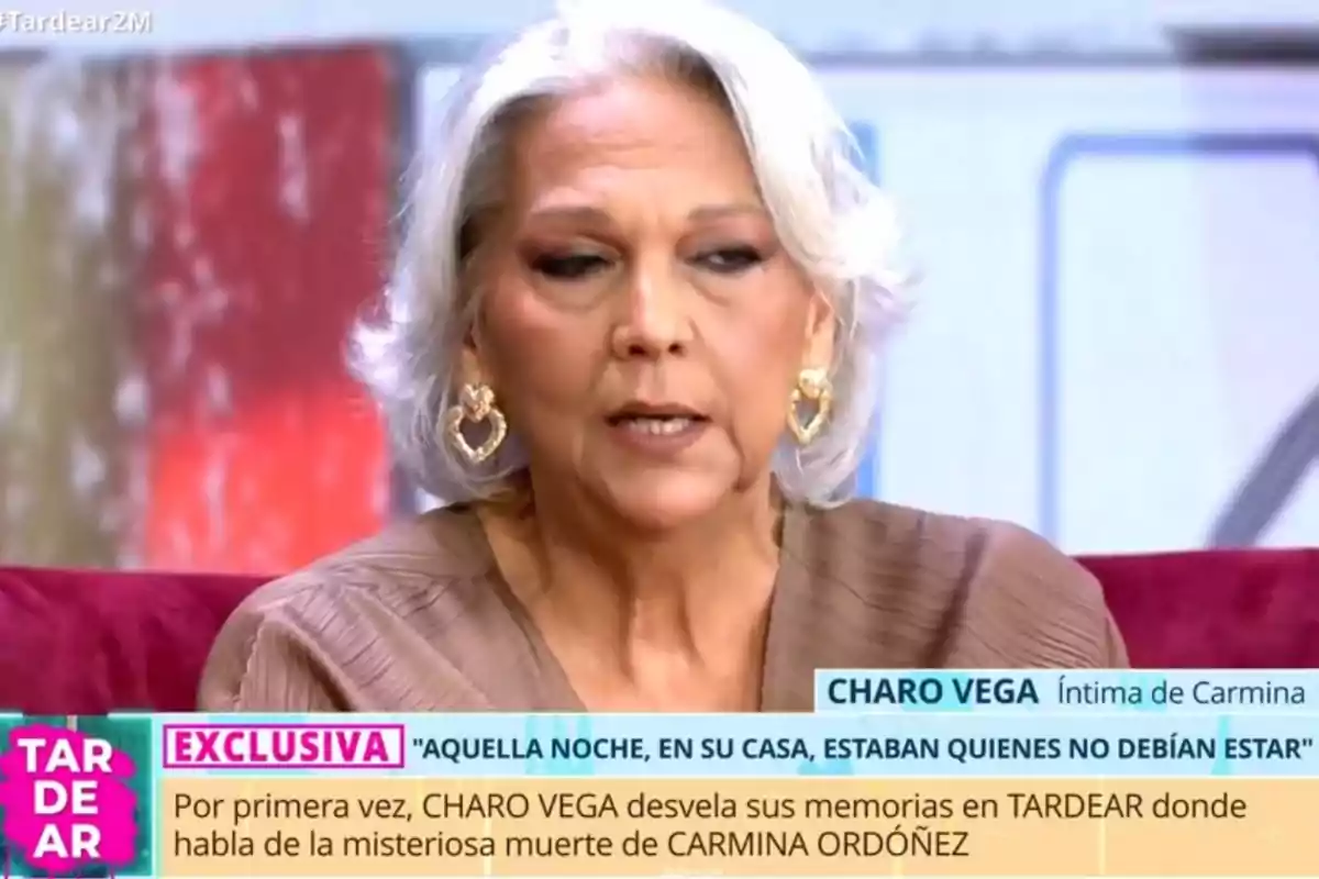 Charo Vega de cabello canoso y corto está sentada en un programa de televisión, lleva pendientes grandes y dorados, y está hablando sobre un tema importante mientras aparece un texto en la parte inferior de la pantalla. Charo Vega de cabello canoso y corto está sentada en un programa de televisión, lleva pendientes grandes y dorados, y está hablando sobre un tema importante mientras aparece un texto en la parte inferior de la pantalla.
