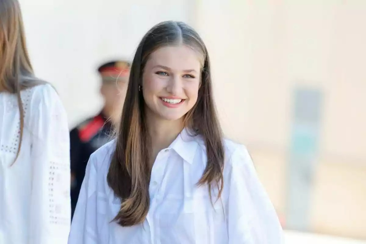 Una joven con cabello largo y lacio sonríe mientras usa una camisa blanca.