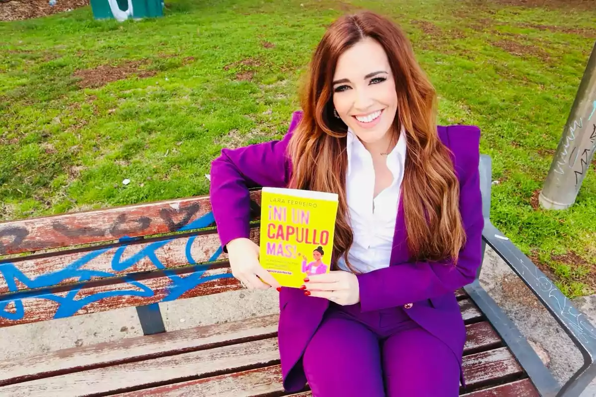 Una persona sentada en un banco de parque, sonriendo y sosteniendo un libro con una portada amarilla.