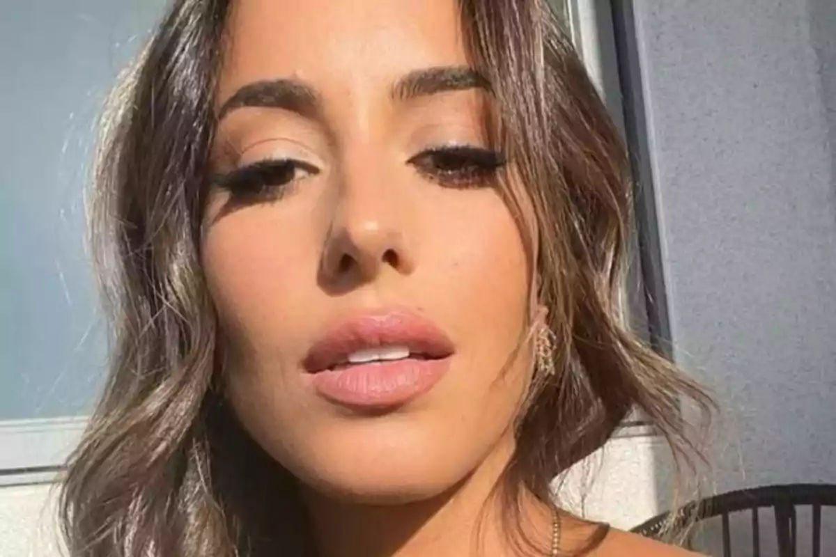 Una persona con cabello castaño y maquillaje suave mira hacia la cámara en un entorno iluminado. Una persona con cabello castaño y maquillaje suave mira hacia la cámara en un entorno iluminado.