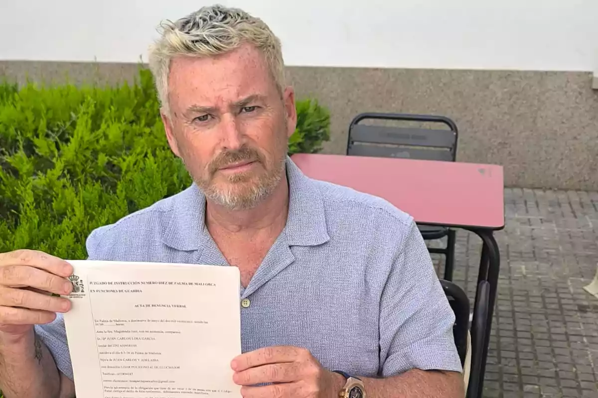 Un hombre con camisa azul sostiene un documento mientras está sentado al aire libre.