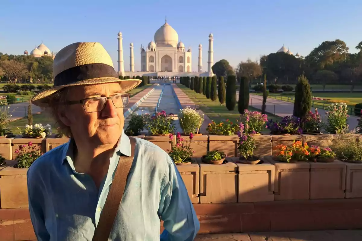 Hombre con sombrero y gafas de pie frente al Taj Mahal al atardecer rodeado de flores y jardines Hombre con sombrero y gafas de pie frente al Taj Mahal al atardecer rodeado de flores y jardines