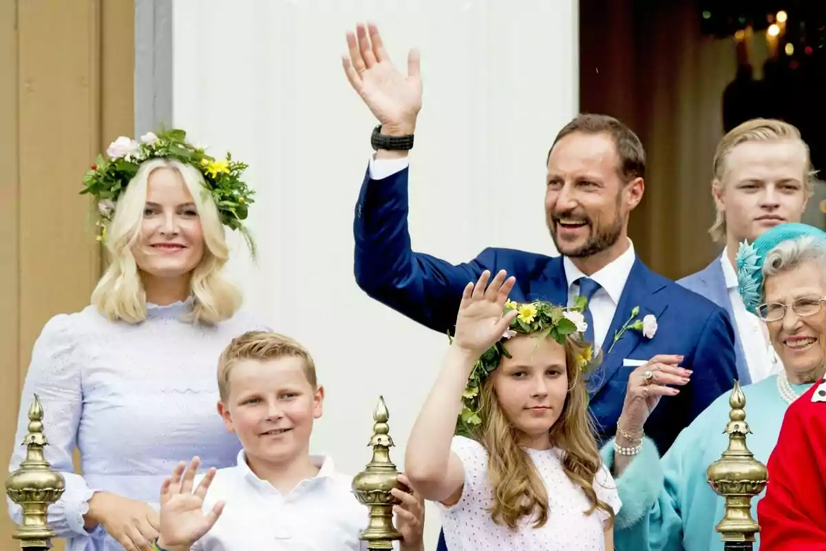 Un grupo de personas sonríe y saluda mientras posan para una foto, algunas llevan coronas de flores y están vestidas de manera elegante. Un grupo de personas sonríe y saluda mientras posan para una foto, algunas llevan coronas de flores y están vestidas de manera elegante.