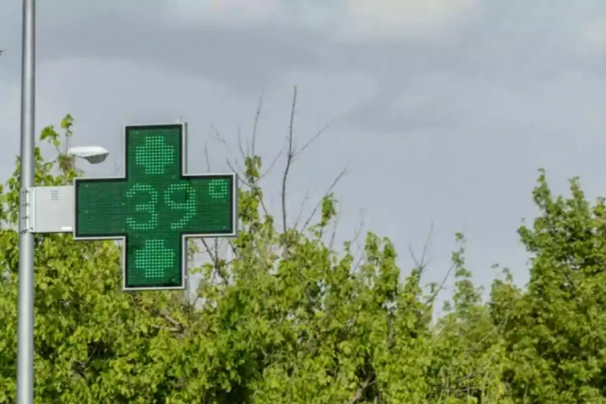 Cruz verde de farmacia con pantalla digital que muestra una temperatura de 39 grados frente a árboles y cielo nublado Cruz verde de farmacia con pantalla digital que muestra una temperatura de 39 grados frente a árboles y cielo nublado
