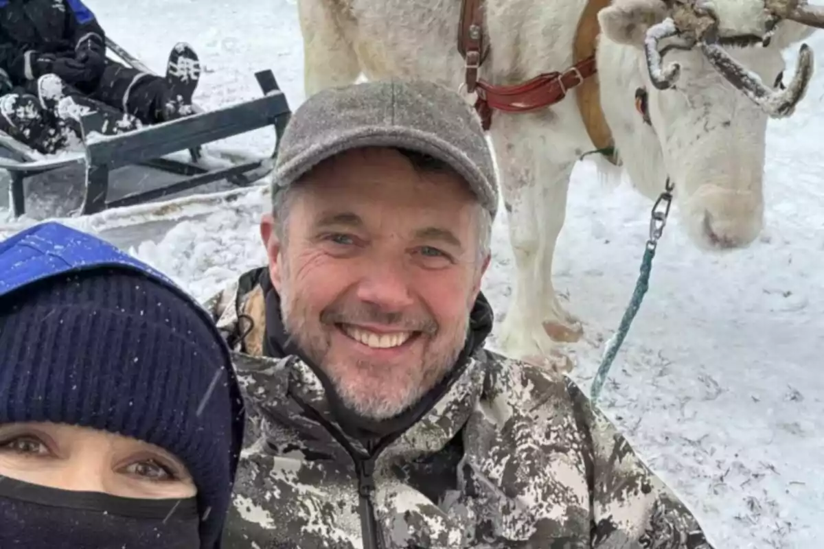 Personas sonrientes posando para una foto en la nieve junto a un reno. Personas sonrientes posando para una foto en la nieve junto a un reno.