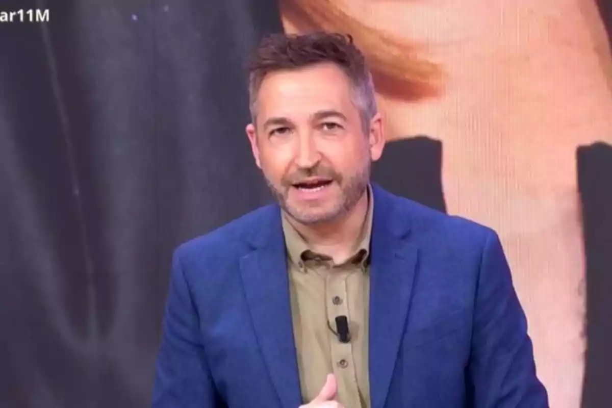 Frank Blanco con barba y cabello corto lleva un traje azul y camisa beige mientras habla frente a una cámara. Frank Blanco con barba y cabello corto lleva un traje azul y camisa beige mientras habla frente a una cámara.