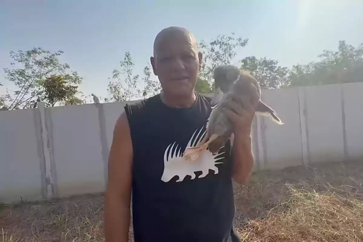 Frank Cuesta sostiene un pato en un entorno al aire libre con árboles y una pared de fondo. Frank Cuesta sostiene un pato en un entorno al aire libre con árboles y una pared de fondo.