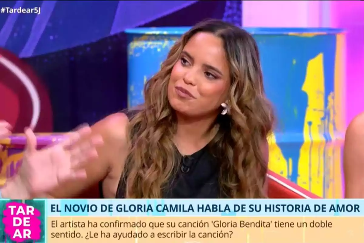 Gloria Camila con cabello largo y ondulado sentada en un plató de televisión colorido durante una entrevista en el programa TardeAR con un rótulo que menciona una historia de amor y una canción llamada Gloria Bendita Gloria Camila con cabello largo y ondulado sentada en un plató de televisión colorido durante una entrevista en el programa TardeAR con un rótulo que menciona una historia de amor y una canción llamada Gloria Bendita