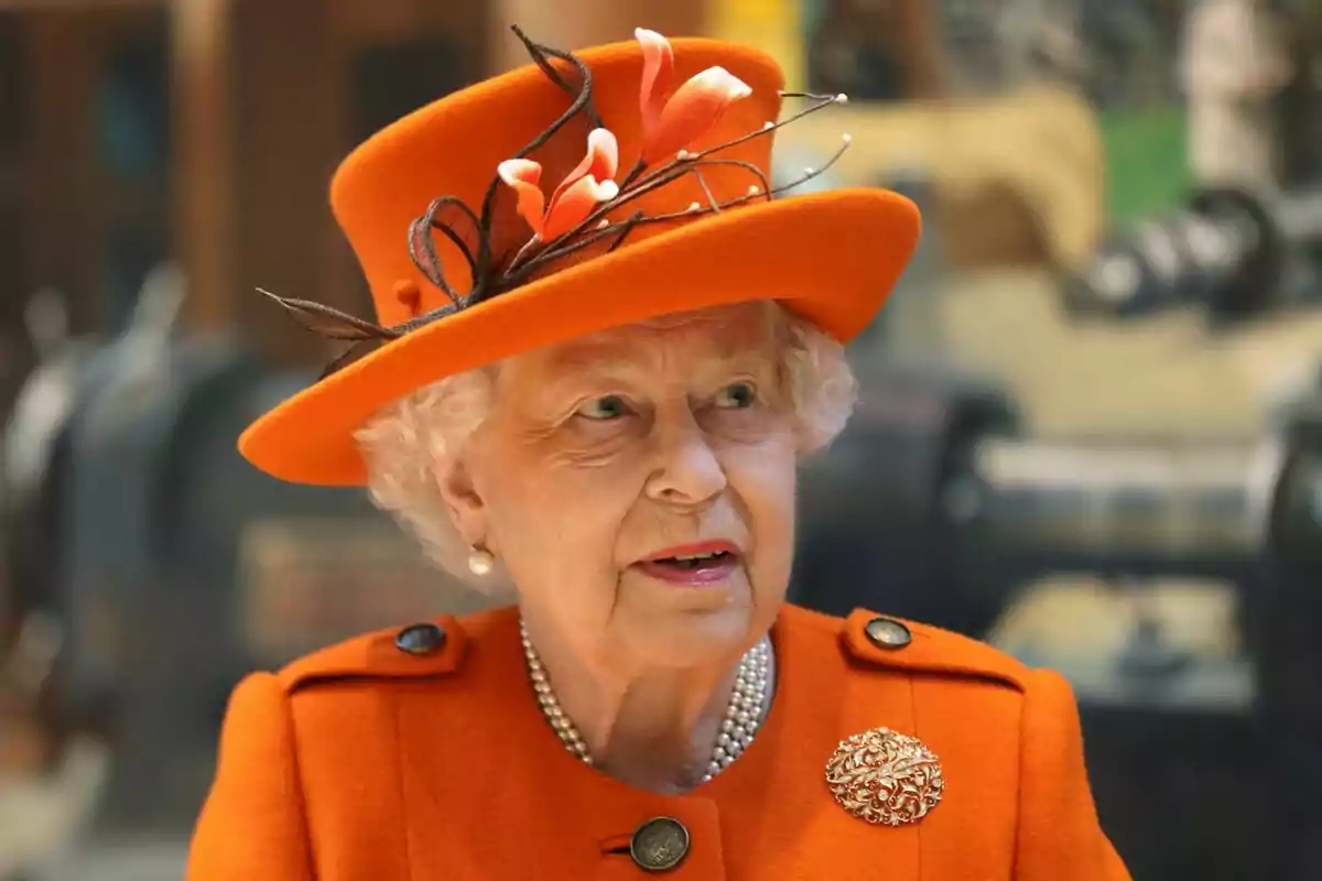 Una persona mayor con sombrero y abrigo naranja adornados con flores y broche. Una persona mayor con sombrero y abrigo naranja adornados con flores y broche.