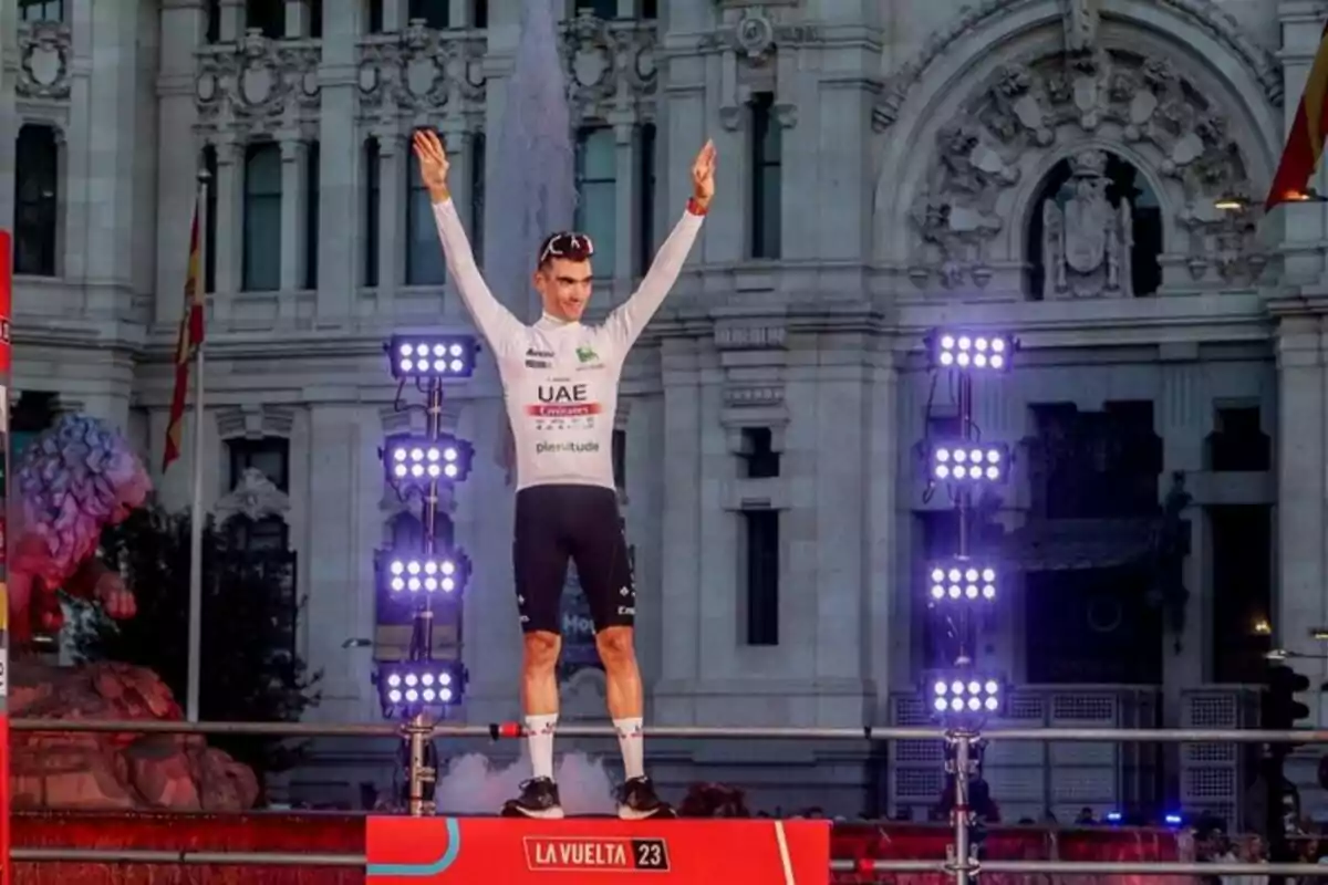 Ciclista celebrando en el podio de La Vuelta 2023 frente a un edificio histórico iluminado.