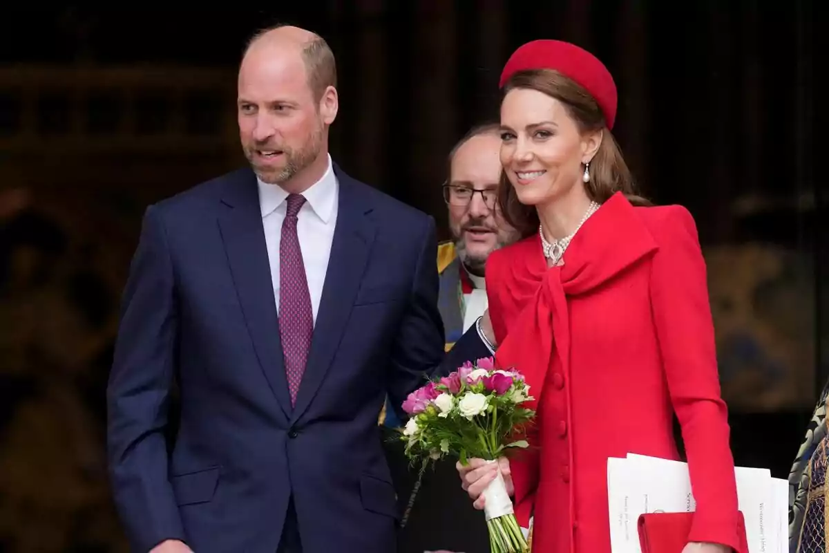 Una pareja elegantemente vestida sale de un edificio, la mujer lleva un ramo de flores y un conjunto rojo. Una pareja elegantemente vestida sale de un edificio, la mujer lleva un ramo de flores y un conjunto rojo.
