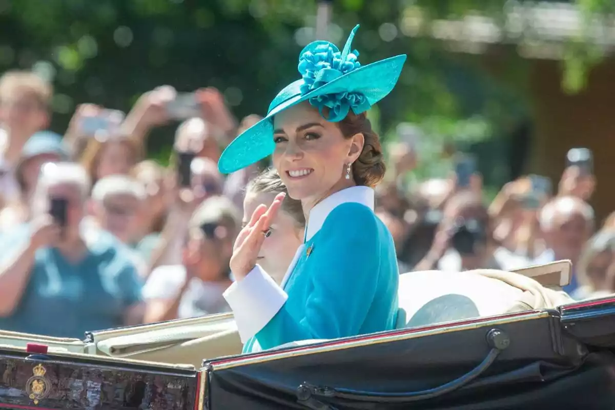 Mujer con sombrero azul sonríe y saluda desde un carruaje durante un evento al aire libre con público de fondo Mujer con sombrero azul sonríe y saluda desde un carruaje durante un evento al aire libre con público de fondo