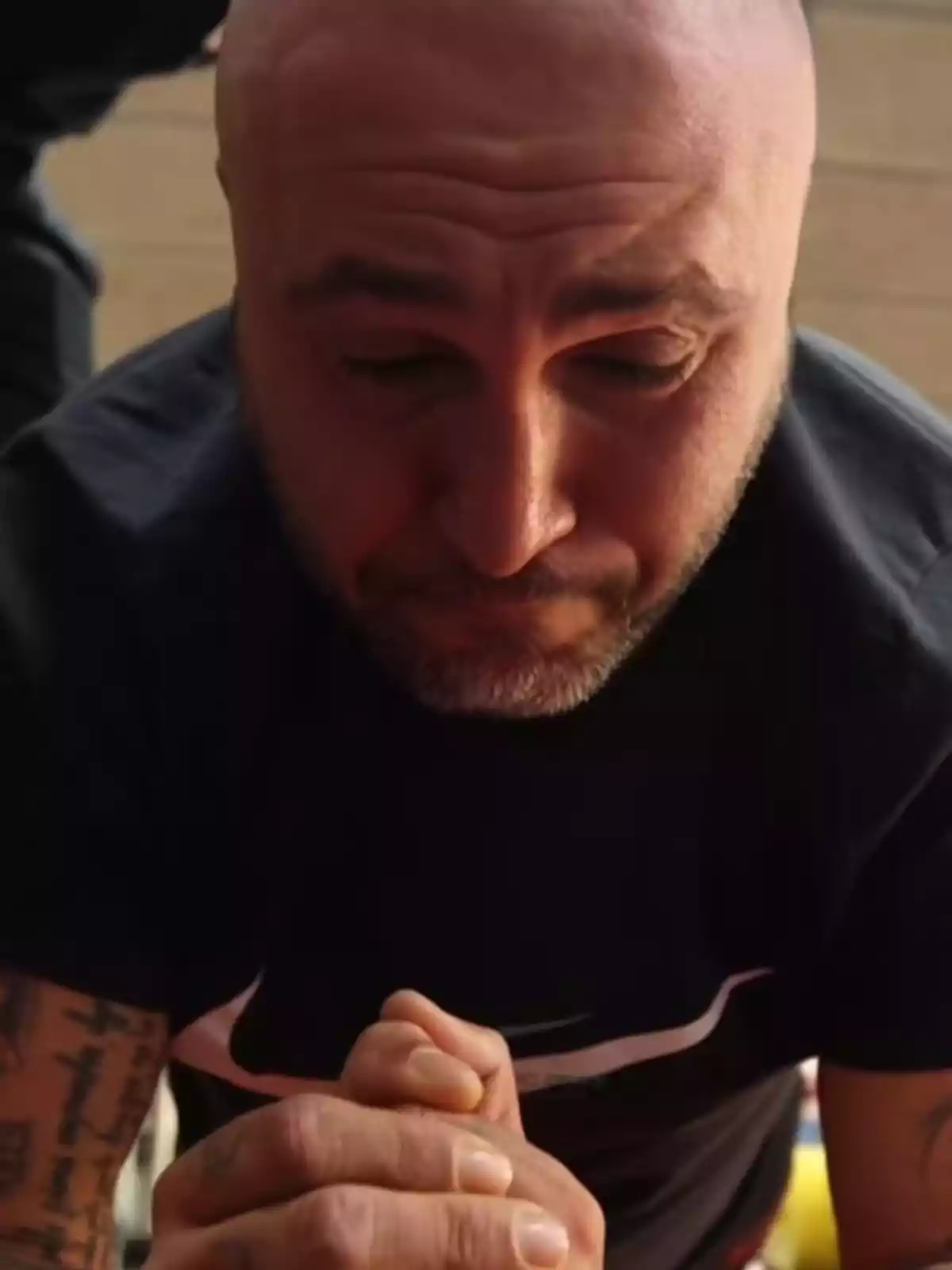Kiko Rivera calvo con barba corta y tatuajes en los brazos está realizando una plancha, con las manos juntas y expresión de esfuerzo.