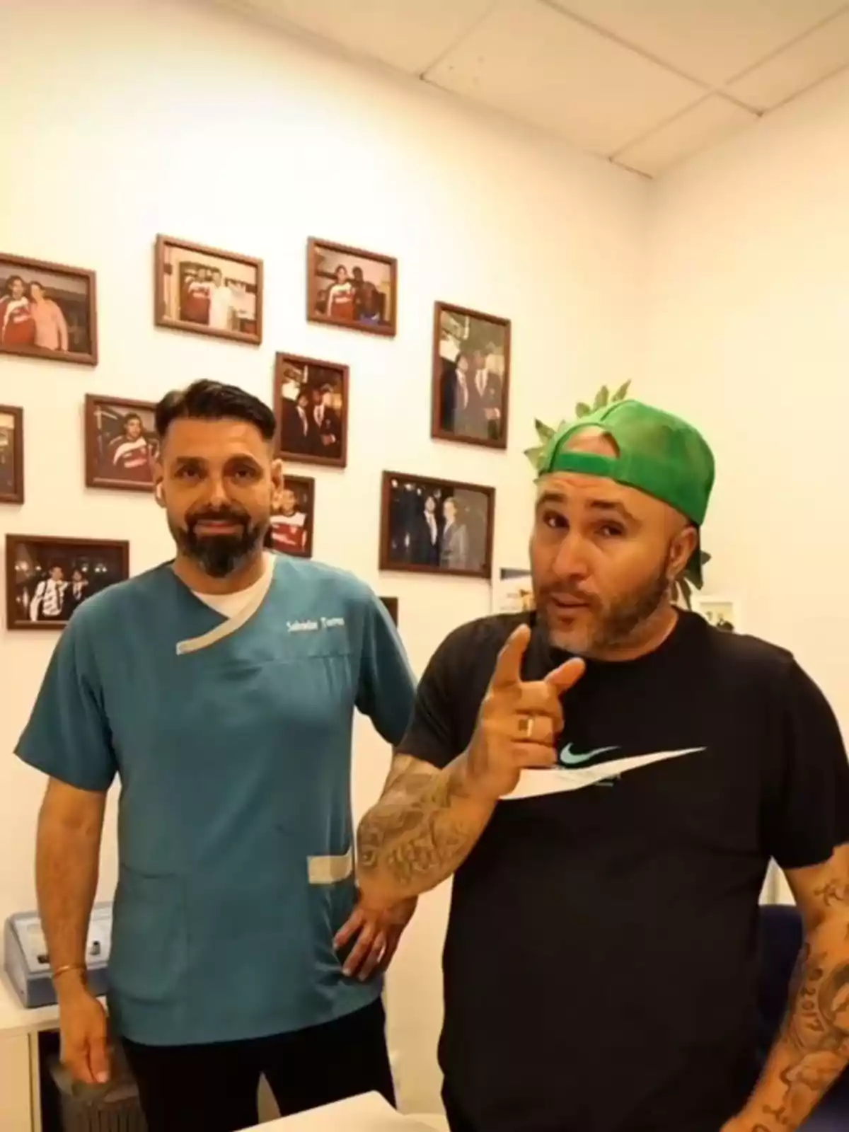 Kiko Rivera y su fisioterapeuta posan en una oficina con varias fotos enmarcadas en la pared, uno lleva uniforme médico y el otro una gorra verde y camiseta negra. Kiko Rivera y su fisioterapeuta posan en una oficina con varias fotos enmarcadas en la pared, uno lleva uniforme médico y el otro una gorra verde y camiseta negra.