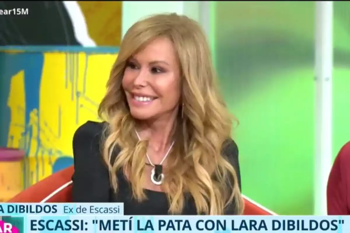 Lara Dibildos sonriente con cabello rubio y ondulado está sentada en un programa de televisión, con un fondo colorido y un texto en la parte inferior de la imagen. Lara Dibildos sonriente con cabello rubio y ondulado está sentada en un programa de televisión, con un fondo colorido y un texto en la parte inferior de la imagen.