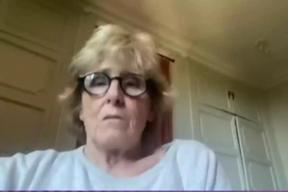 Mercedes Milá con gafas y cabello rubio aparece en una videollamada desde una habitación con paredes claras y un armario al fondo. Mercedes Milá con gafas y cabello rubio aparece en una videollamada desde una habitación con paredes claras y un armario al fondo.