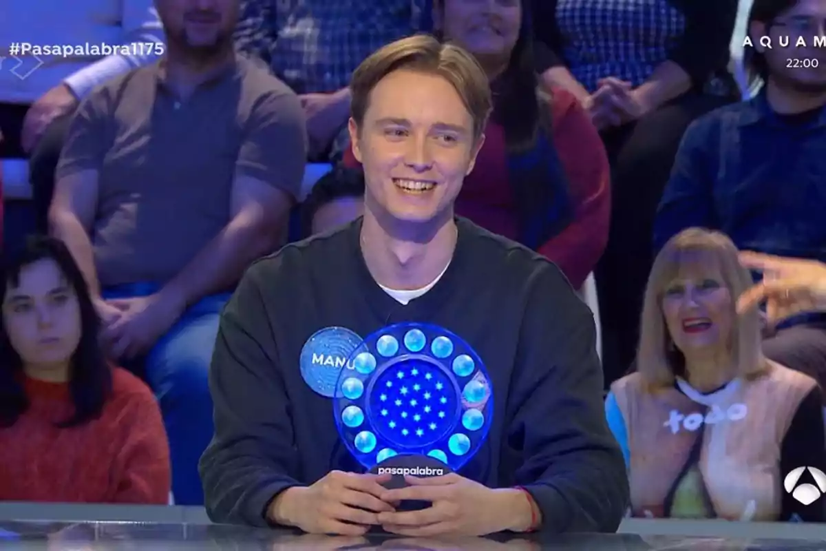 Manu sonriente en un programa de televisión con un público de fondo. Manu sonriente en un programa de televisión con un público de fondo.
