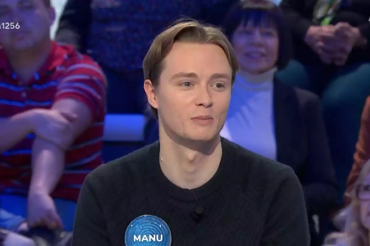 Manu joven con cabello claro y suéter oscuro está sentado en un estudio de televisión con público al fondo. Manu joven con cabello claro y suéter oscuro está sentado en un estudio de televisión con público al fondo.
