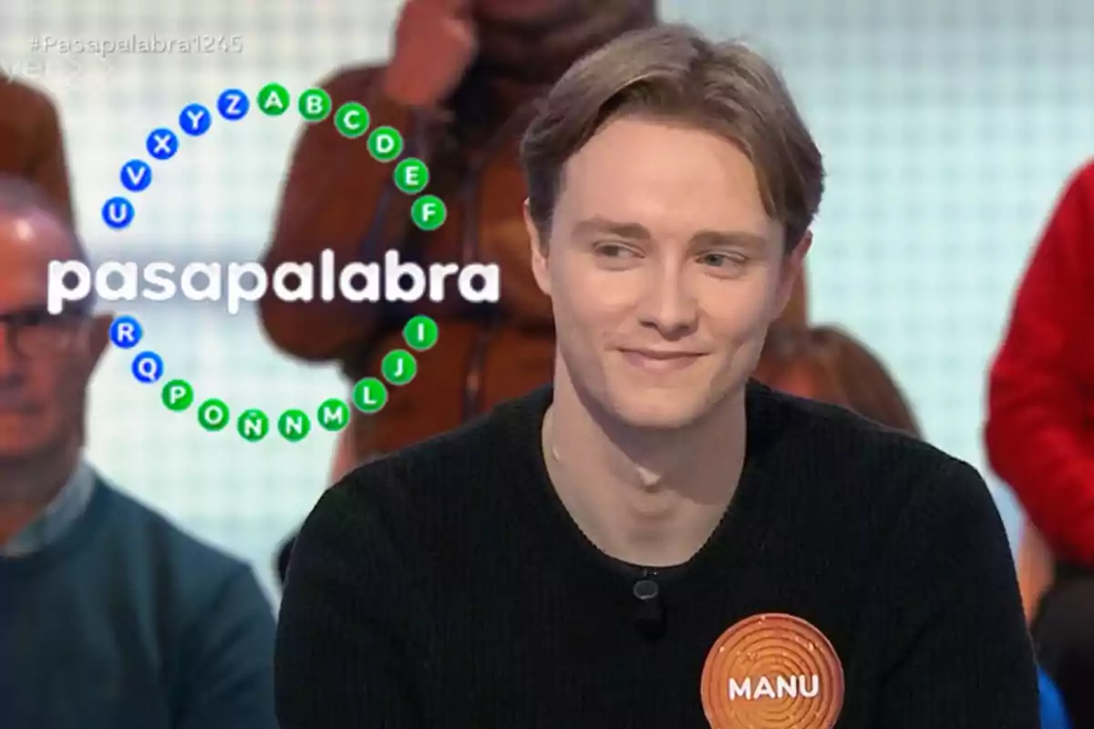 Manu sonríe mientras participa en un programa de televisión llamado "Pasapalabra", con un círculo de letras en el fondo.