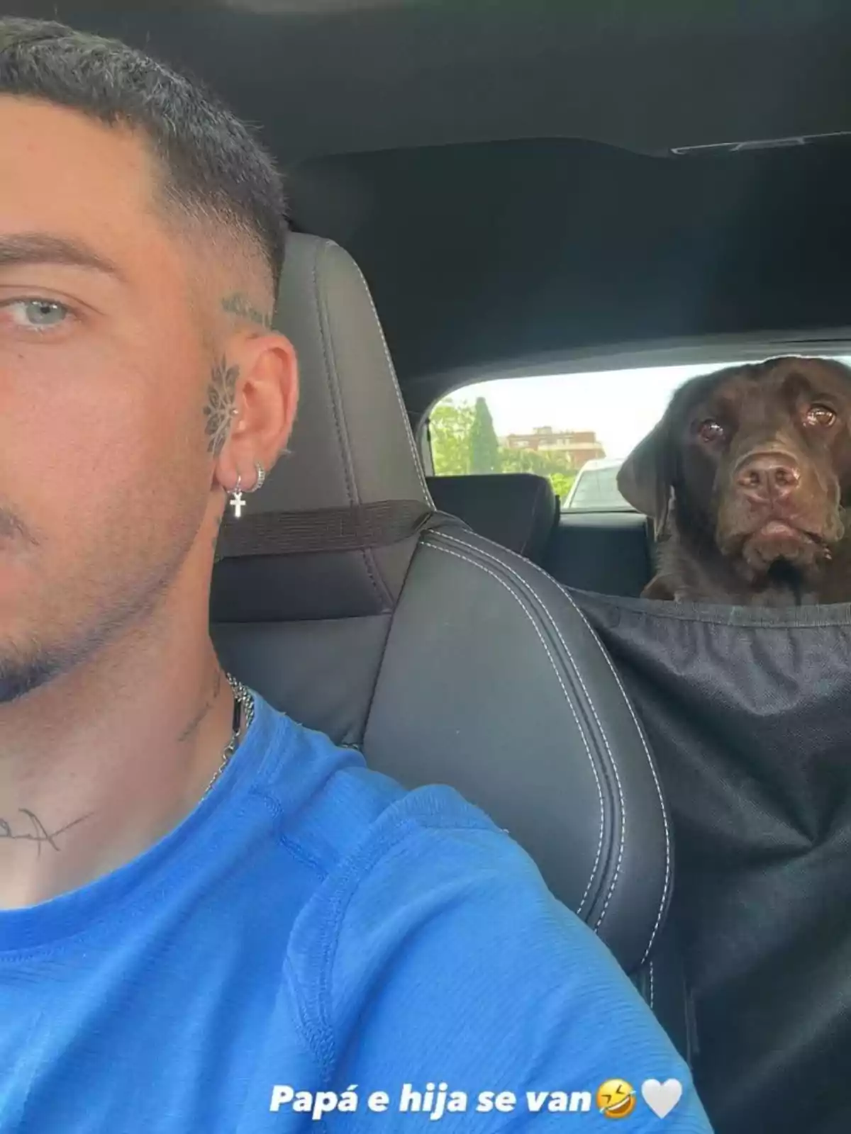 Manuel Bedmar con tatuajes y una camiseta azul está en el asiento del conductor de un coche, mientras un perro marrón está sentado en el asiento trasero. Manuel Bedmar con tatuajes y una camiseta azul está en el asiento del conductor de un coche, mientras un perro marrón está sentado en el asiento trasero.
