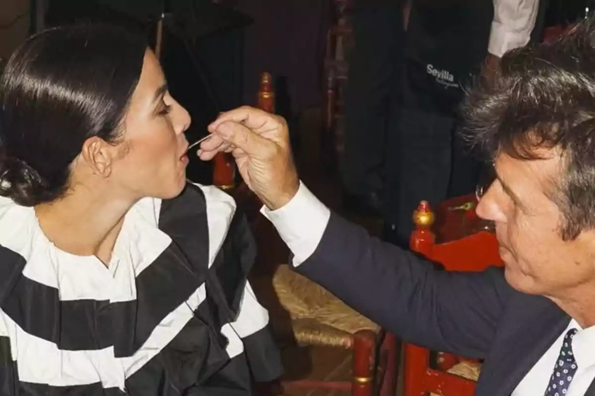 Manuel Díaz ‘El Cordobés’ está alimentando a Virginia Troconis con una cuchara en un ambiente que parece ser un evento social. Manuel Díaz ‘El Cordobés’ está alimentando a Virginia Troconis con una cuchara en un ambiente que parece ser un evento social.