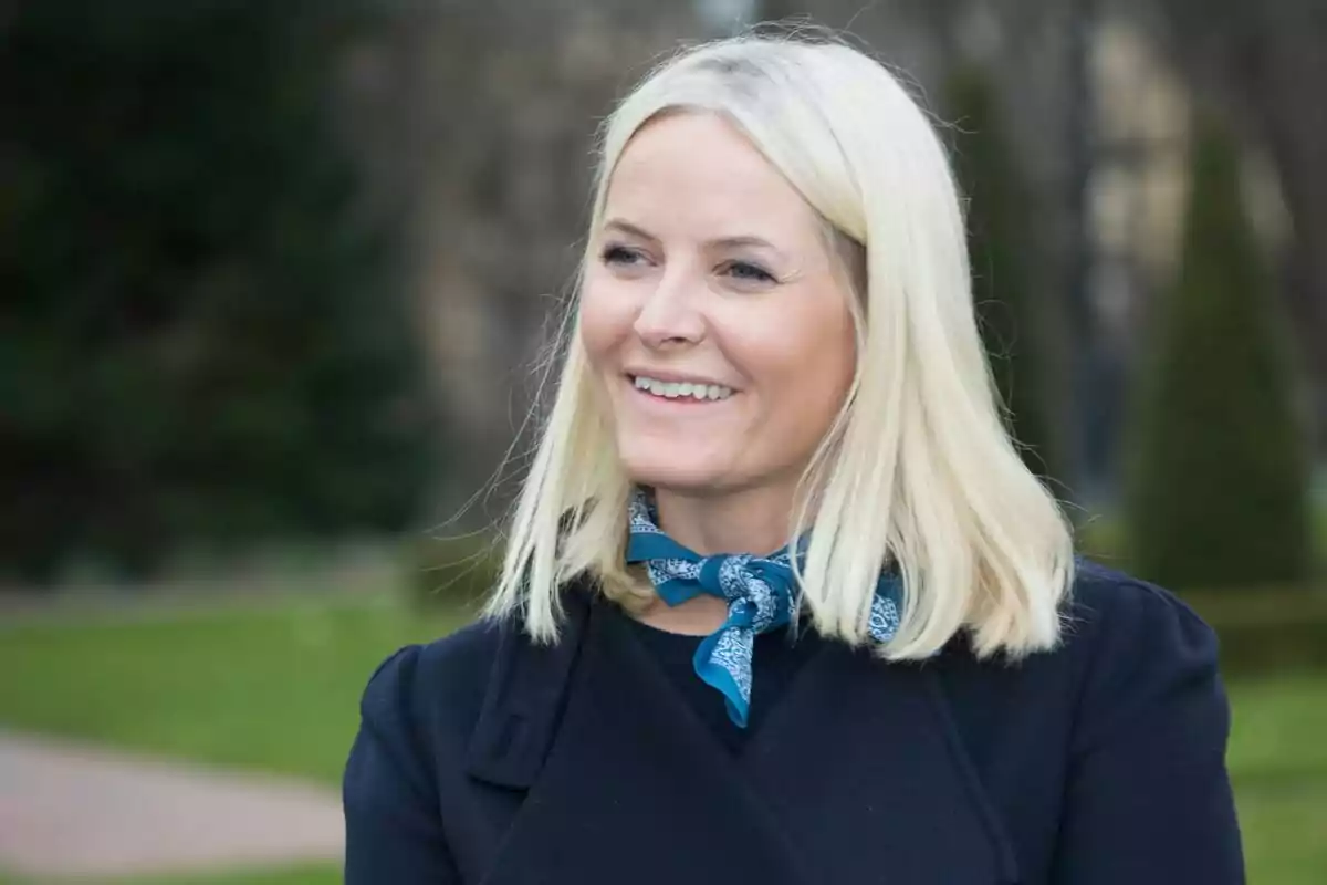 Una mujer rubia sonriendo al aire libre con un pañuelo azul alrededor del cuello. Una mujer rubia sonriendo al aire libre con un pañuelo azul alrededor del cuello.