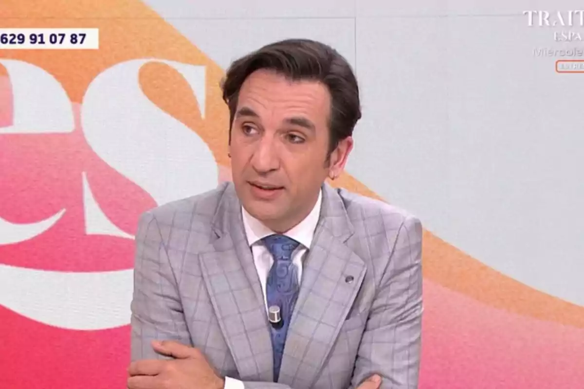 Miguel Lago con traje gris y corbata azul aparece en un programa de televisión con un fondo colorido. Miguel Lago con traje gris y corbata azul aparece en un programa de televisión con un fondo colorido.