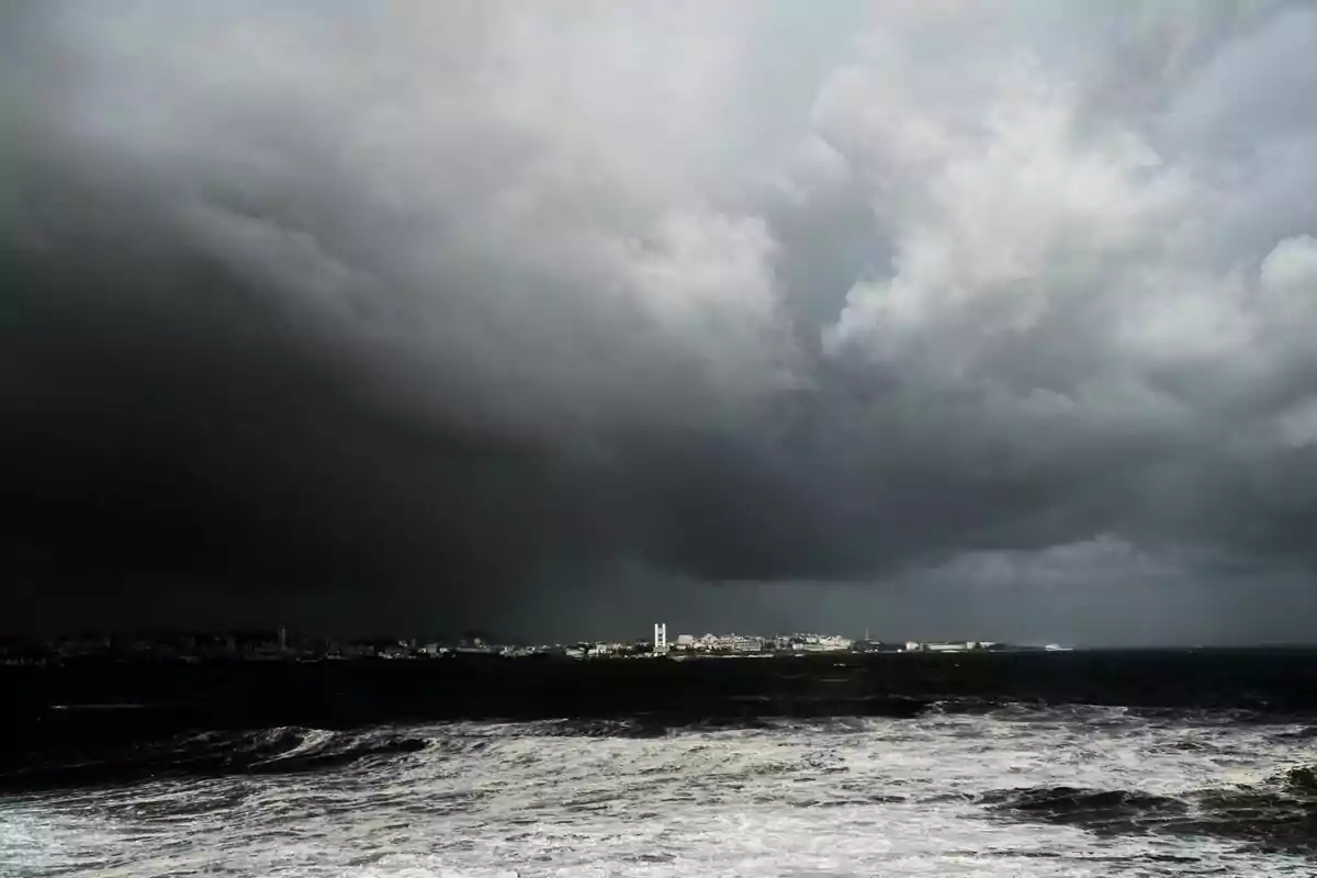 Cielo nublado y oscuro sobre un mar agitado con una ciudad en el horizonte.